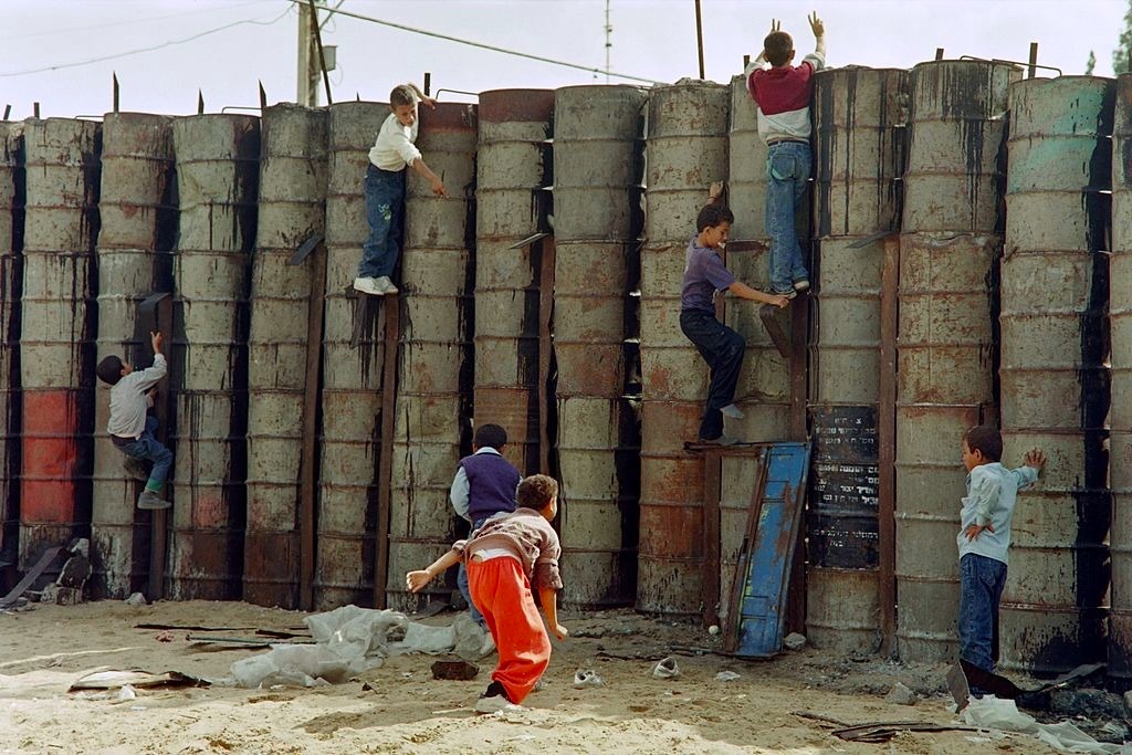 أطفال يتسلقون حاجزاً نصبته قوات الاحتلال عند أحد مداخل مخيم الشاطئ في غزّة، 1989، المصدر:AFP
