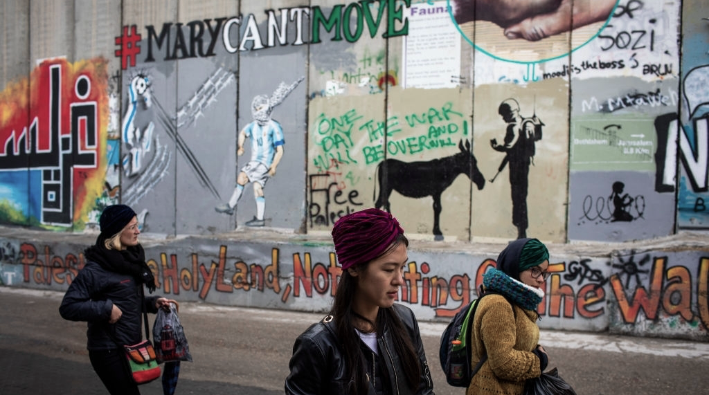 سيّاح يمرّون أمام الجدار الإسرائيلي في بيت لحم. (Getty Images).