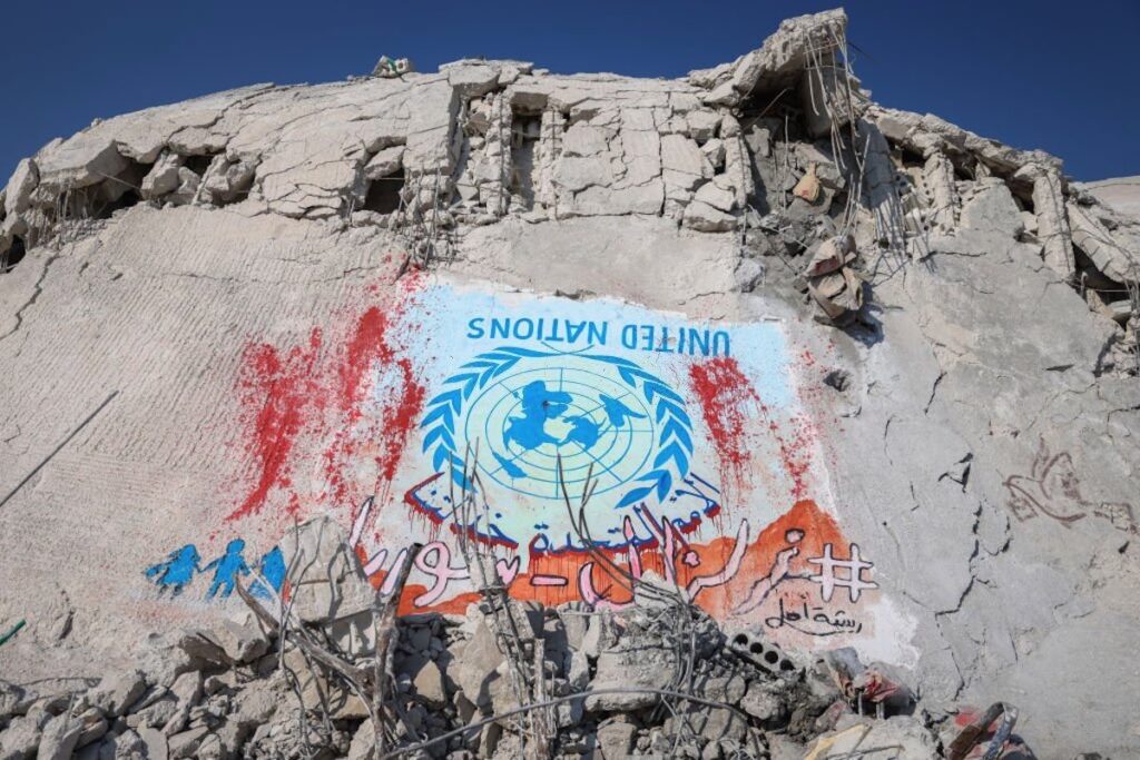 شعار الأمم المتحدة مرسوماً على ركام أحد المنازل في بلدة سرمدا في محافظة إدلب، كاحتجاج على غياب المساعدات الأممية. (عدسة: أنس الخربوطلي/ Getty Images).