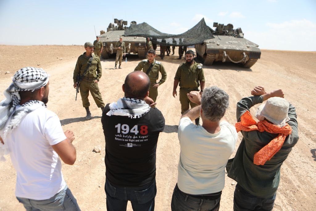مسافر يطا، جنوب الخليل، 22 حزيران 2022، مجموعة من الفلسطينيين يقفون محتجين أمام آليات عسكرية لجيش الاحتلال خلال إجرائها تدريبات بالقرب من أراضيهم في المسافر. (مأمون وزوز/ وكالة الأناضول).