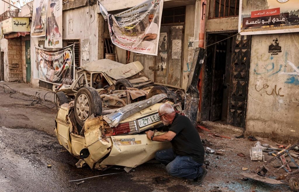 رجل فلسطينيّ يتفقد سيارة في مخيّم جنين، دمّرتها قوات الاحتلال الإسرائيلي خلال اقتحامها للمكان مطلع تموز/ يوليو 2023، في عملية عسكريّة تعمّدت خلالها تدمير البنية التحتيّة فجرفت الشوارع وهدمت المنازل ودمرت شبكات المياه وغيرها. (وكالة الصحافة الفرنسية).