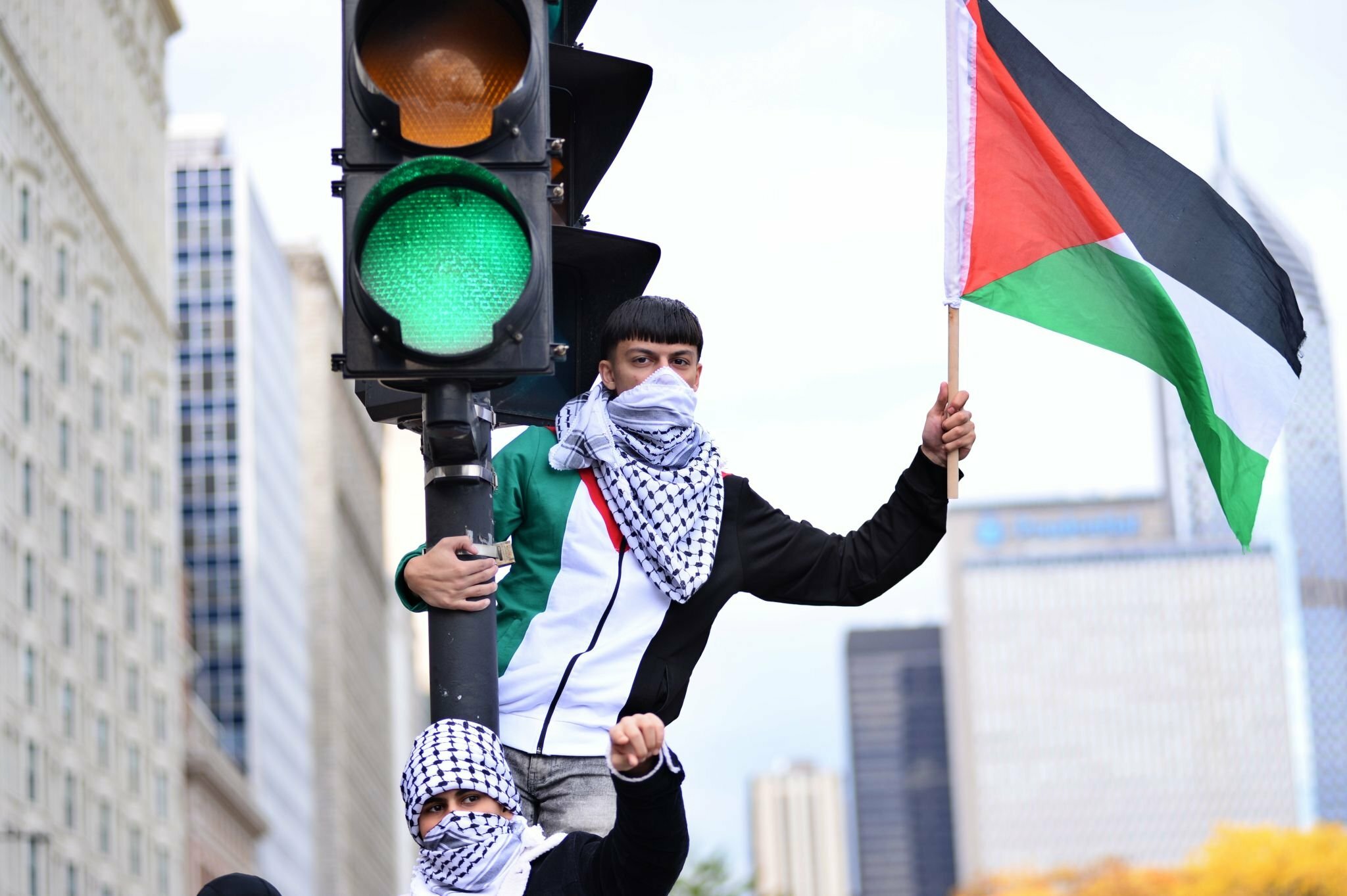 شيكاغو، إلينوي، الولايات المتحدة، 21 تشرين الأول/ أكتوبر 2023، شاب يرفع العلم الفلسطينيّ وآخر ملثم بالكوفية الفلسطينيّة خلال تظاهرة شاركها فيها عشرات الآلاف في المدينة للتعبير عن تضامنهم مع فلسطين، وللمطالبة بوقف العدوان الإسرائيلي على غزة. (وكالة الأناضول).